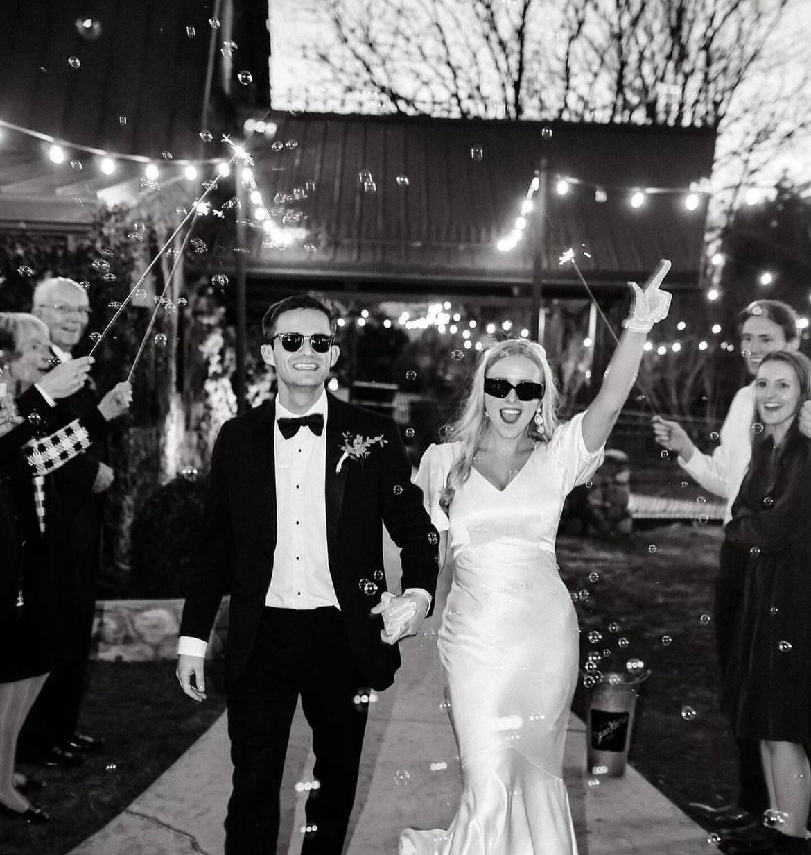 black and white picture of bride and groom exiting wedding wearing sunglasses with sparklers