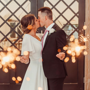 Man in suit and lady in white wedding dress kissing and holding 20 inch sparklers with bright gold sparks