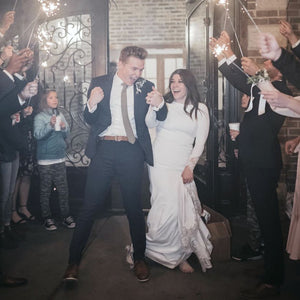 Bride and groom joyfully exiting wedding venue in Utah as guests celebrate with extra long sparklers for wedding sendoff.