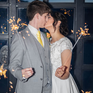 Man in gray suit and lady in white wedding dress kissing and holding 20 inch low smoke wedding sparklers