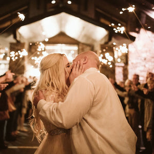 Bride and groom leaving wedding venue surrounded by guests holding extra long sparklers for a wedding sendoff.