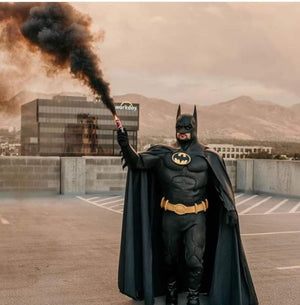 Man dressed in black Batman costume holding black smoke bombs for photography in hand in air