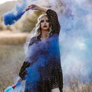 Blue Color Smoke Bomb held by lady wearing black gypsy dress in green grass