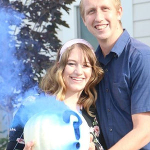 Husband and expecting wife with gender reveal bomb emitting blue smoke from pumpkin