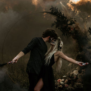 Man and sexy woman faces painted as skeletons holding black smoke bombs for Halloween photo shoot