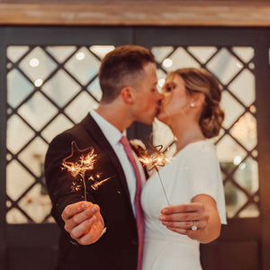 Man and woman dressed in wedding clothes each holding Star Sparklers