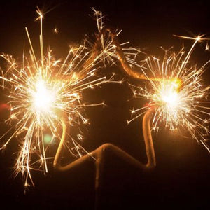 close up of star Sparkler lit emitting gold sparks against dark background