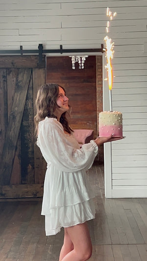 Girl celebrating birthday looking at pink ombre cake with silver sparkler candle