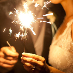 Close up of bride and groom holding 10-Inch Multi-Colored Sparklers emitting gold sparks against dark background