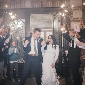 Newly married couple exiting wedding venue with guests holding extra long sparklers for wedding sendoff