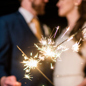 "Extra long sparklers for wedding sendoff, held by a hand with golden sparks illuminating the night sky in celebration."