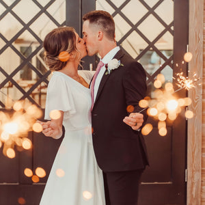 Bride and groom holding extra long sparklers for wedding sendoff in front of the elegant venue, creating a magical and festive atmosphere.