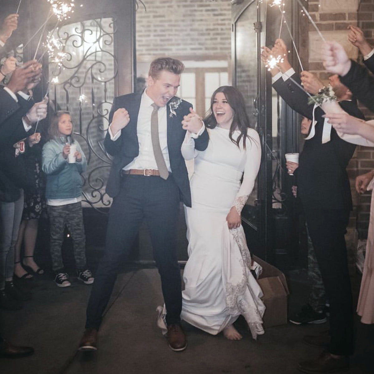 &quot;Bride and groom joyfully exiting wedding ceremony as guests celebrate with low smoke wedding sparklers, creating a magical atmosphere.&quot;