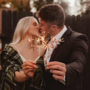 Lady and man kissing each holding lit star sparkler in hands outside