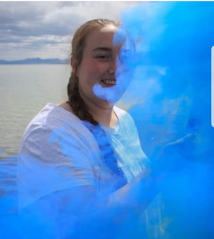 Girl in white shirt with smoke bombs for photography and blue smoke bomb creating blue background for graduation pictures