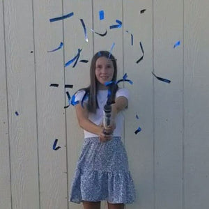 Young girl celebrating birthday holding handheld confetti shooting out blue strips paper confetti