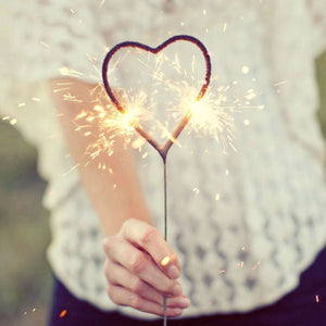 Close up of lady wearing short sleeve white sweater holding heart sparkler in one hand