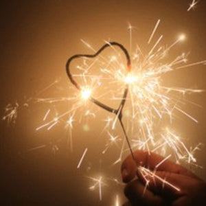 Close up of heart sparkler being held in hand emitting bright gold sparks with a gold background