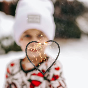 Little boy in Valentine's pajamas holding a heart sparkler, surrounded by snow in the background, creating a magical winter celebration.