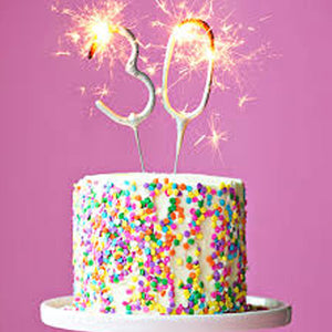 Number sparklers placed on a number 30 birthday cake, emitting gold sparks, creating a festive atmosphere for birthdays.